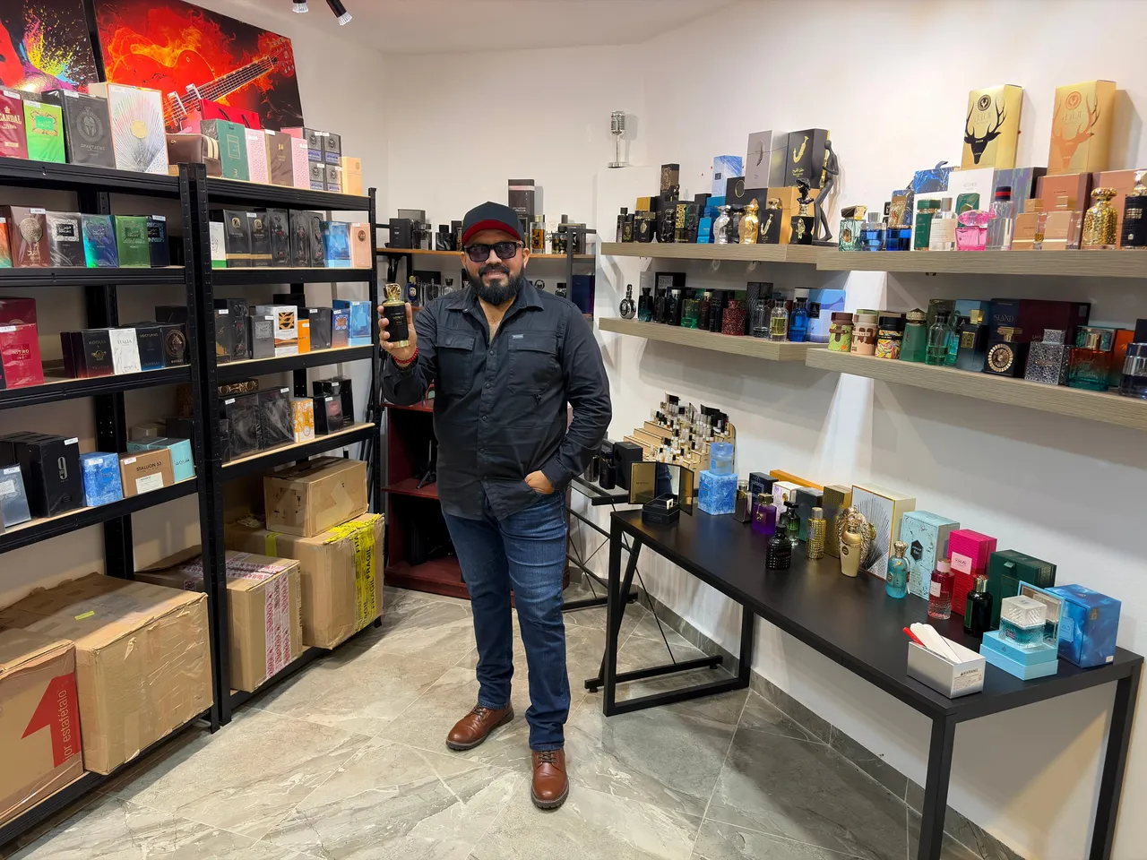 Jesús, dueño de El Barbón de los Perfumes, sosteniendo una fragancia entre los anaqueles de su tienda en Mérida